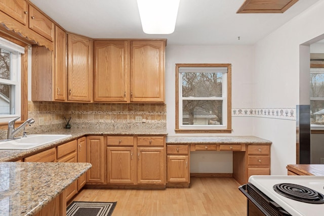 kitchen with light wood finished floors, tasteful backsplash, light stone counters, built in desk, and a sink