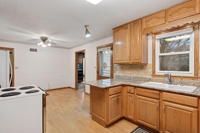 kitchen with visible vents, a sink, white appliances, a peninsula, and light wood finished floors