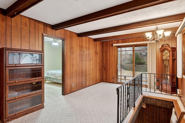 corridor with an upstairs landing, a notable chandelier, beam ceiling, carpet, and wood walls