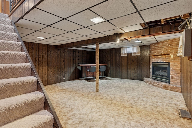 basement featuring a brick fireplace, stairway, wooden walls, and carpet