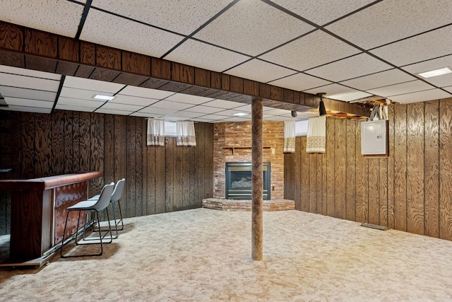 basement with electric panel, wood walls, a brick fireplace, and carpet