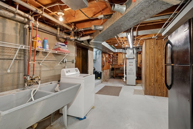 unfinished below grade area featuring a sink, heating unit, washer / dryer, and freestanding refrigerator