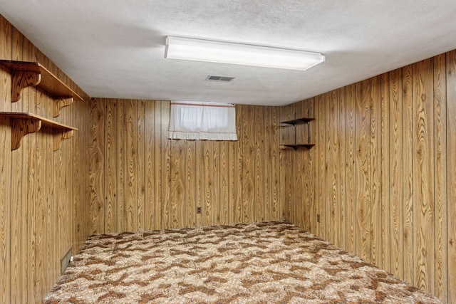 basement with visible vents, wood walls, and a textured ceiling