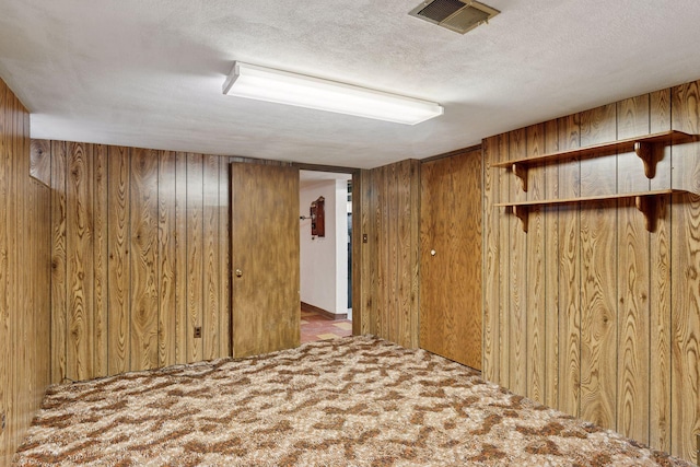 finished basement with visible vents, wood walls, a textured ceiling, and carpet floors