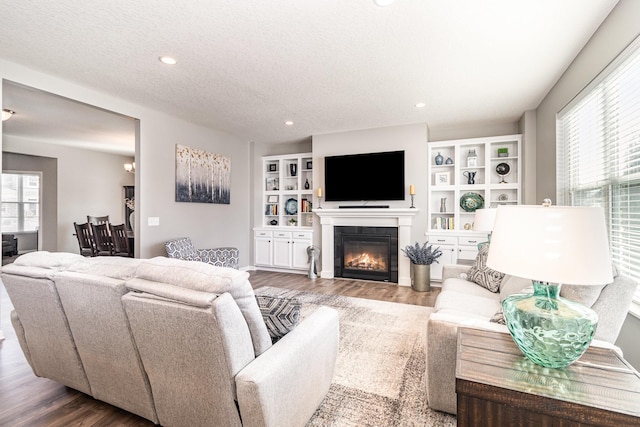 living room with recessed lighting, a textured ceiling, a glass covered fireplace, and wood finished floors