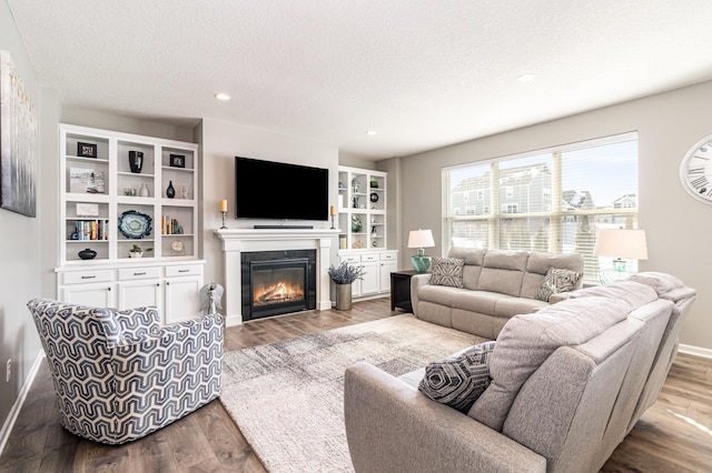 living area featuring a textured ceiling, a glass covered fireplace, recessed lighting, baseboards, and wood finished floors