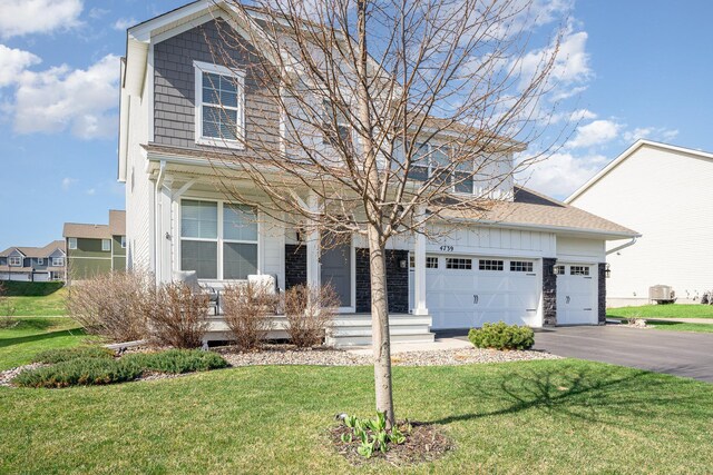 traditional-style house with a porch, an attached garage, driveway, and a front yard