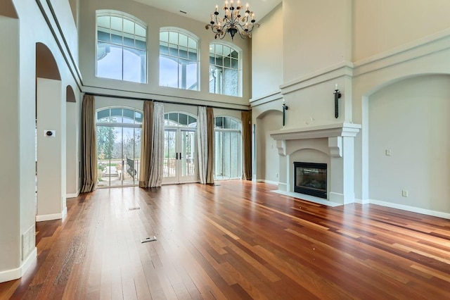 unfurnished living room featuring a fireplace with flush hearth, arched walkways, baseboards, and hardwood / wood-style flooring