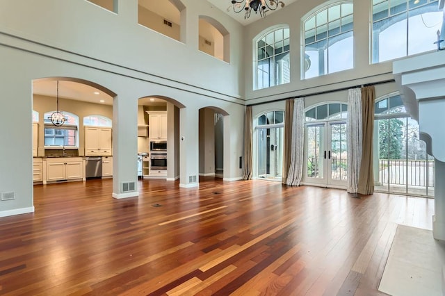 unfurnished living room with dark wood-style floors, arched walkways, a chandelier, and a sink