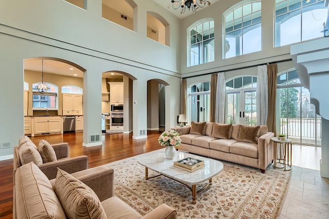 living area featuring arched walkways, a notable chandelier, wood finished floors, visible vents, and baseboards