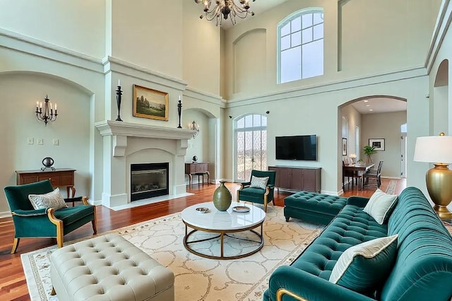 living area with arched walkways, a notable chandelier, a fireplace with flush hearth, wood finished floors, and baseboards