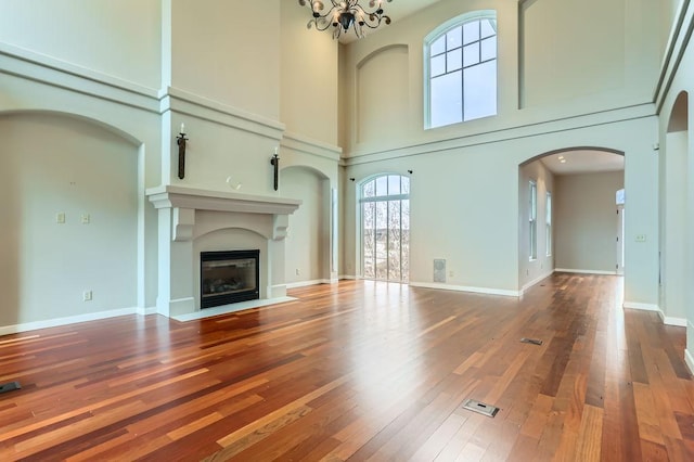 unfurnished living room with a notable chandelier, a fireplace with flush hearth, baseboards, and hardwood / wood-style floors