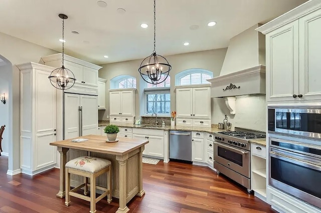 kitchen with built in appliances, wooden counters, a notable chandelier, and custom range hood