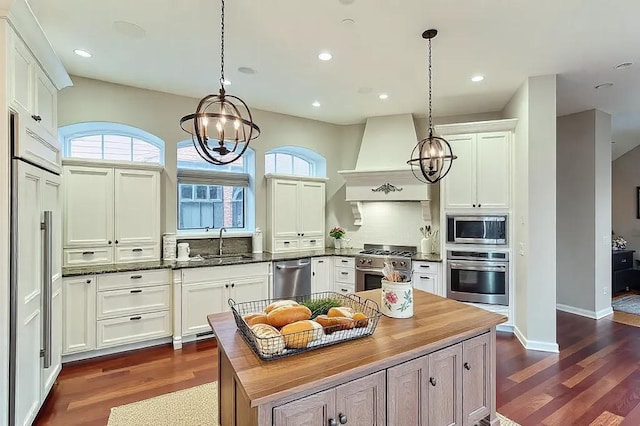 kitchen featuring built in appliances, premium range hood, a sink, wooden counters, and a wealth of natural light