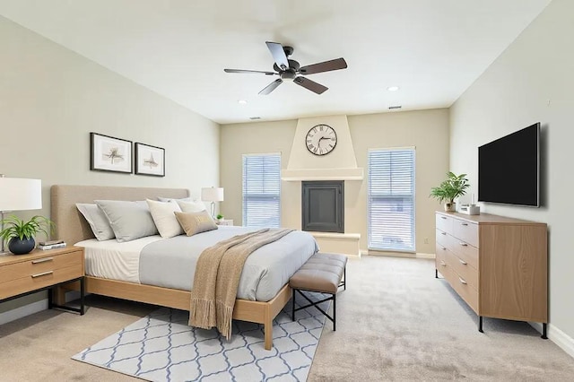 bedroom with ceiling fan, baseboards, a glass covered fireplace, and light colored carpet