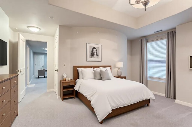 bedroom with baseboards, visible vents, a tray ceiling, and light colored carpet