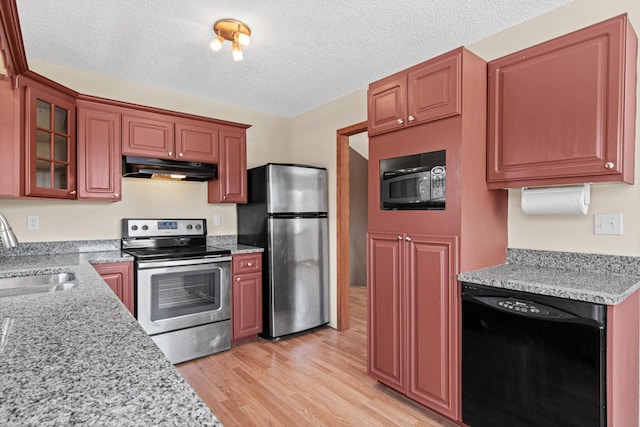 kitchen featuring light wood-style flooring, glass insert cabinets, under cabinet range hood, black appliances, and a sink