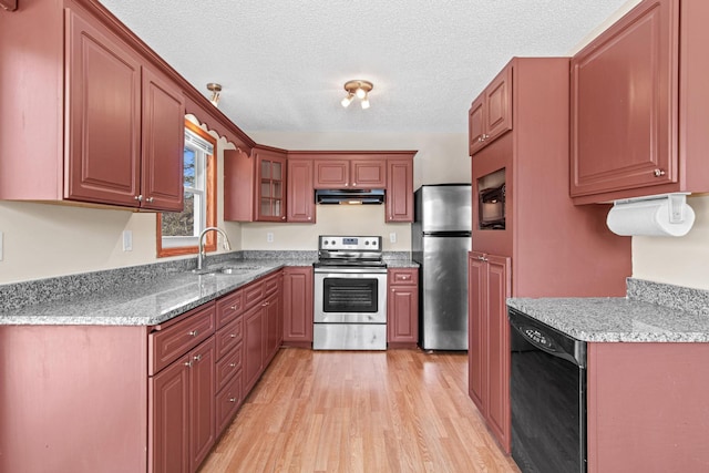 kitchen with light wood-style flooring, appliances with stainless steel finishes, a textured ceiling, under cabinet range hood, and a sink