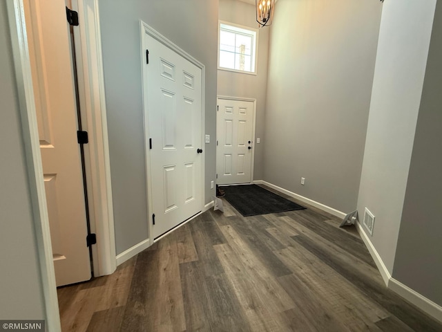 doorway to outside with dark wood-style flooring, visible vents, a towering ceiling, and baseboards