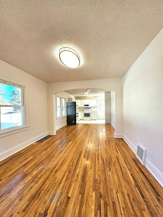 unfurnished living room with a textured ceiling, wood finished floors, visible vents, and baseboards