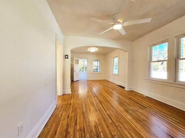 empty room with baseboards, visible vents, arched walkways, a textured ceiling, and light wood-style floors