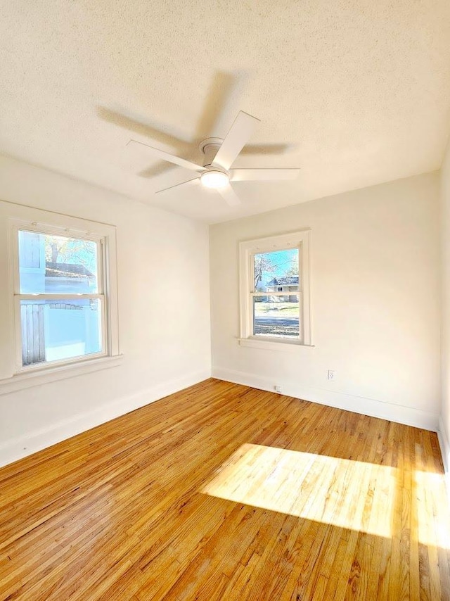 empty room with a textured ceiling, wood finished floors, a ceiling fan, and baseboards