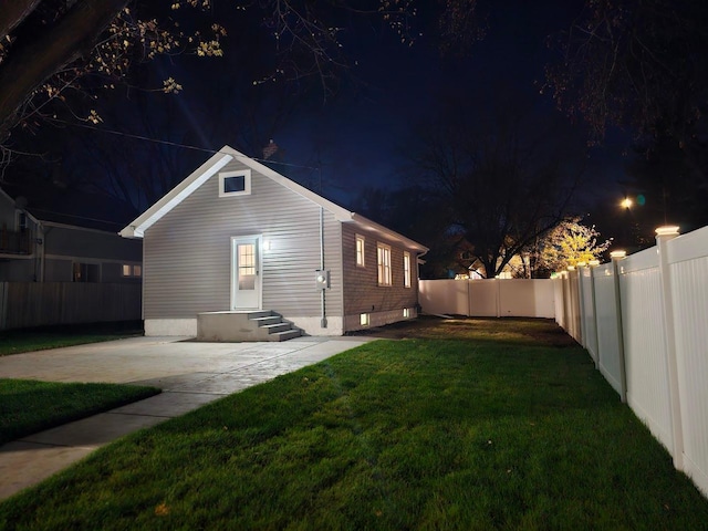 back of house at night featuring a patio area, a fenced backyard, and a yard