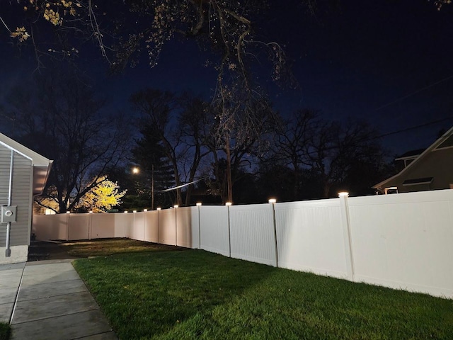 yard at night featuring a fenced backyard