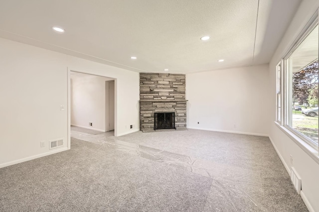 unfurnished living room with light carpet, recessed lighting, a stone fireplace, baseboards, and a textured ceiling