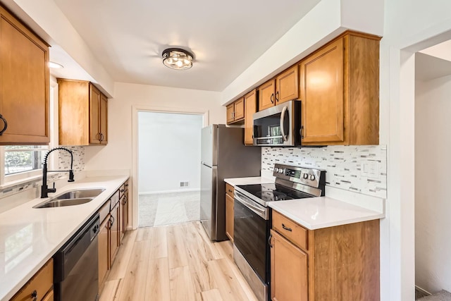 kitchen with stainless steel appliances, a sink, decorative backsplash, brown cabinetry, and light countertops