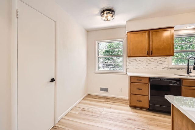 kitchen with black dishwasher, light wood-style flooring, light countertops, brown cabinetry, and a sink