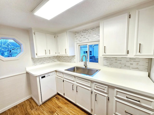 kitchen with white dishwasher, a sink, white cabinetry, light wood-style floors, and light countertops