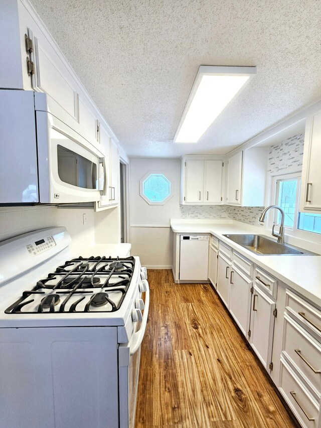 kitchen featuring light wood-style flooring, white appliances, a sink, white cabinets, and light countertops