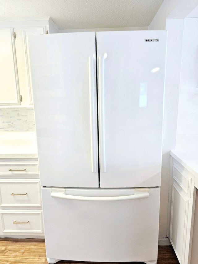 interior details featuring light wood-style floors, freestanding refrigerator, light countertops, and white cabinetry