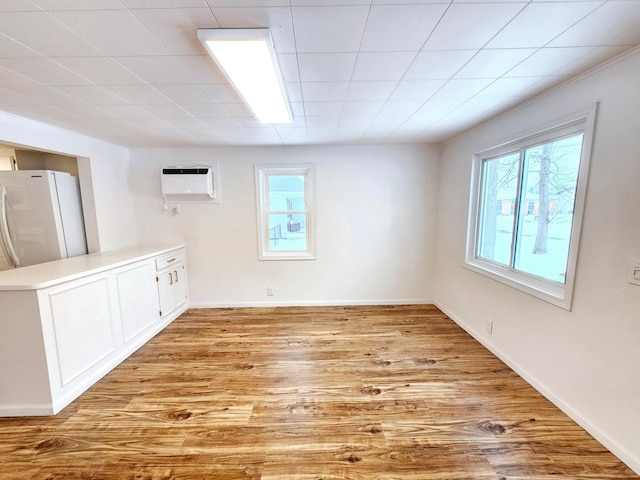 empty room featuring light wood-style floors, an AC wall unit, and baseboards