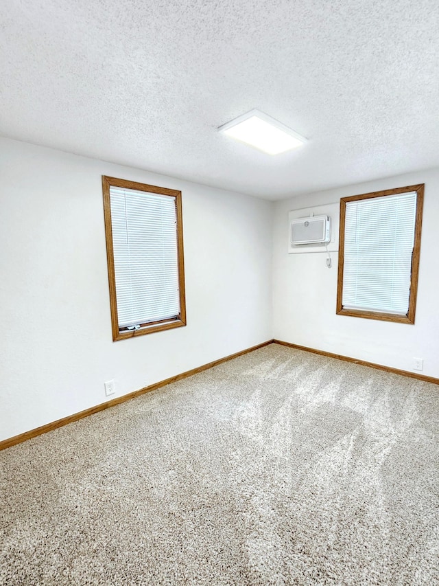 empty room featuring a textured ceiling, carpet floors, a wall mounted air conditioner, and baseboards