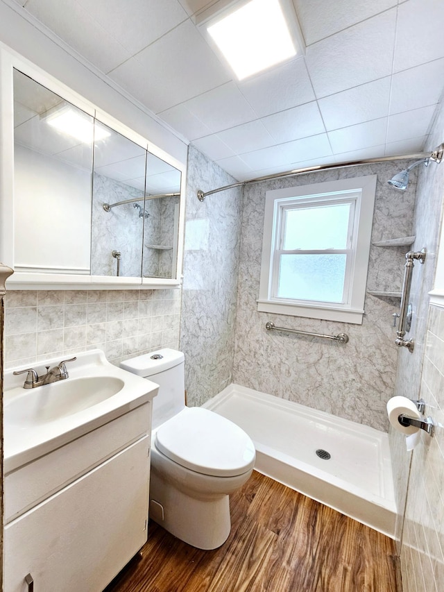 bathroom featuring toilet, wood finished floors, vanity, tile walls, and a stall shower