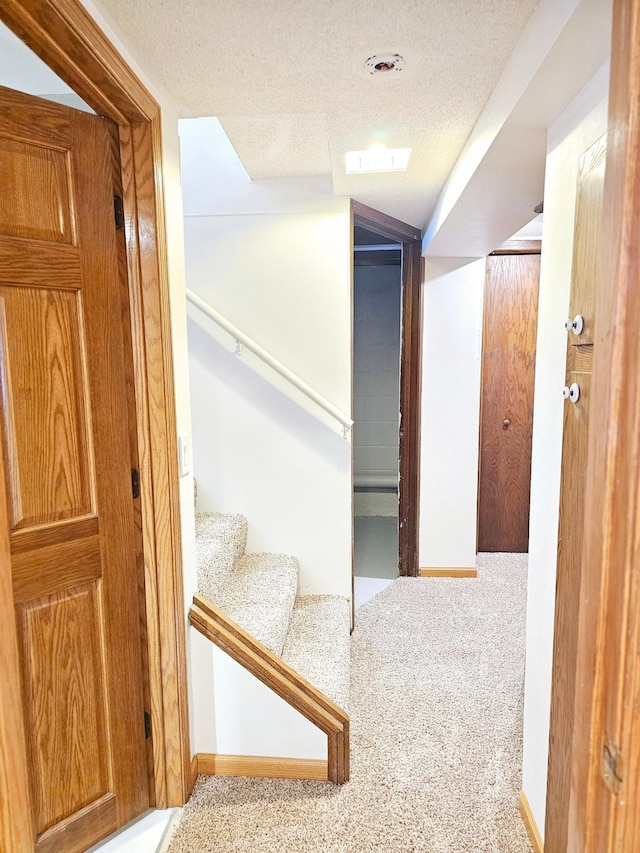 hall with light carpet, a textured ceiling, stairs, and baseboards