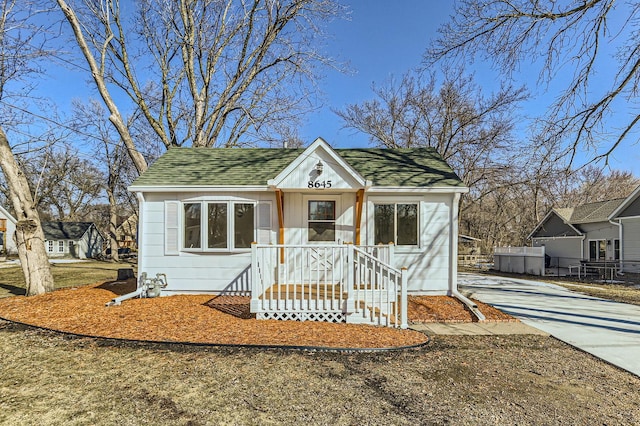 bungalow-style home with concrete driveway, fence, and a shingled roof