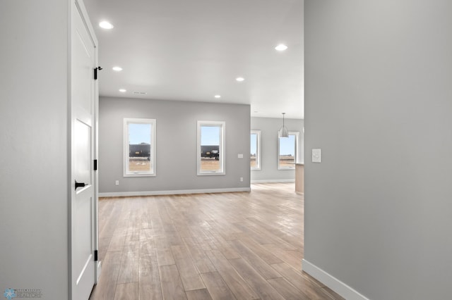 unfurnished living room featuring light wood-style floors, recessed lighting, a healthy amount of sunlight, and baseboards