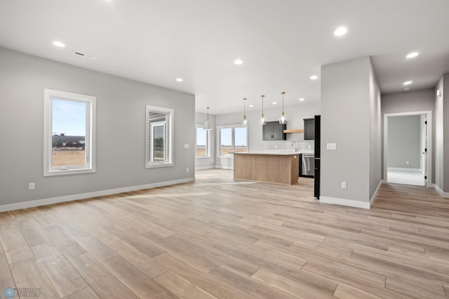 unfurnished living room featuring light wood-type flooring, baseboards, a sink, and recessed lighting