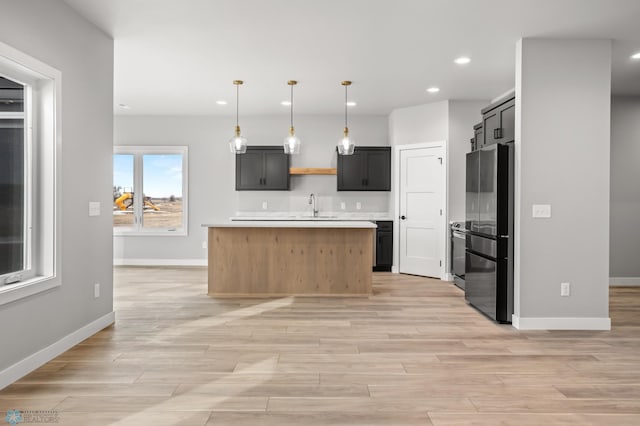 kitchen featuring freestanding refrigerator, hanging light fixtures, light countertops, light wood-style floors, and a sink