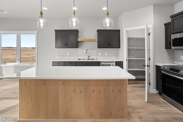 kitchen with a center island, decorative light fixtures, light countertops, appliances with stainless steel finishes, and a sink