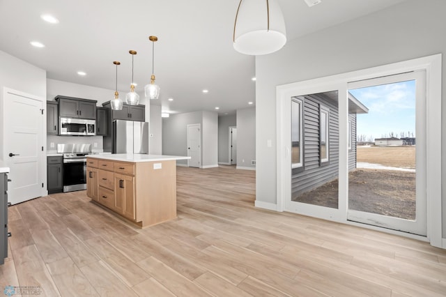 kitchen featuring appliances with stainless steel finishes, decorative light fixtures, a center island, light countertops, and light brown cabinetry