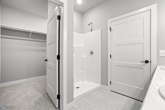 full bathroom featuring double vanity, a shower stall, a spacious closet, and baseboards