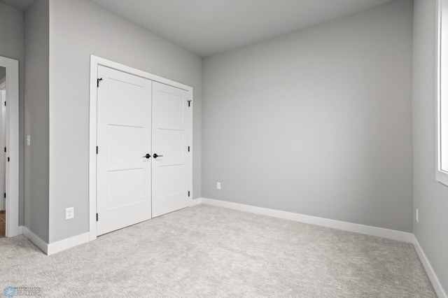 unfurnished bedroom with a closet, light colored carpet, and baseboards