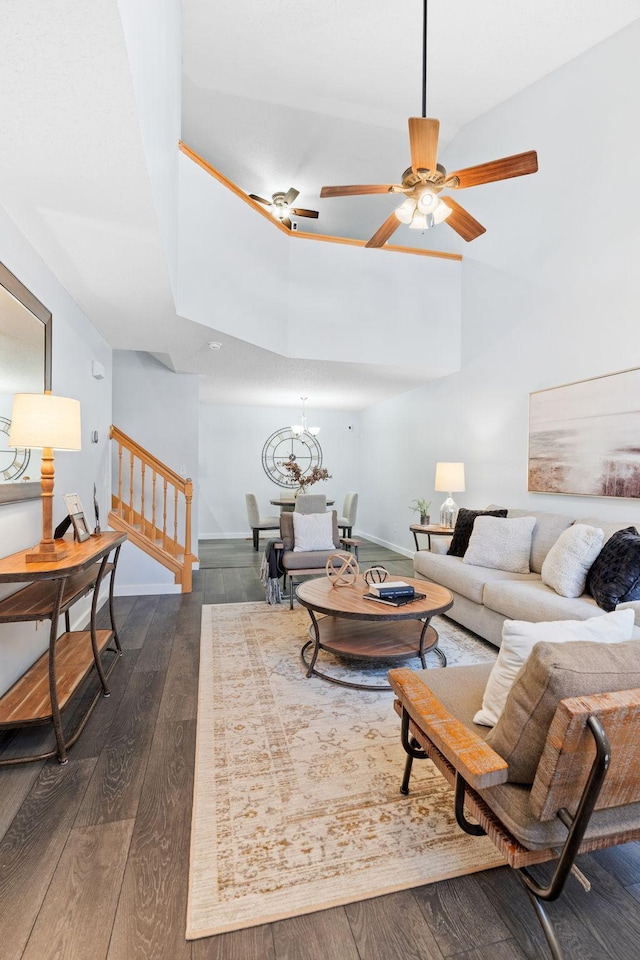 living area with baseboards, dark wood finished floors, stairs, a towering ceiling, and ceiling fan with notable chandelier