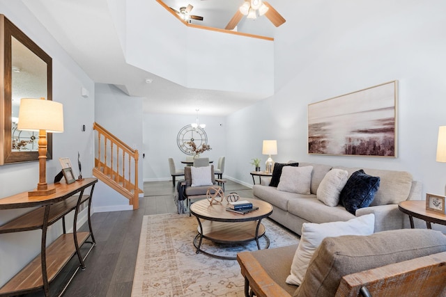 living area featuring dark wood-type flooring, ceiling fan with notable chandelier, a high ceiling, baseboards, and stairs