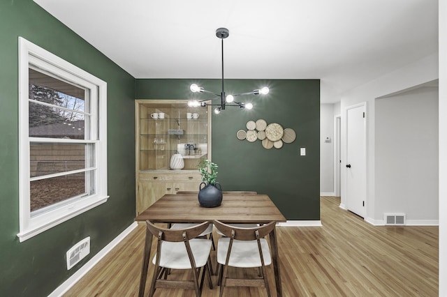 dining area with plenty of natural light, baseboards, visible vents, wood finished floors, and a chandelier