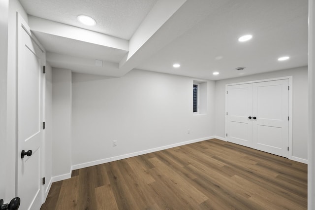 finished below grade area featuring a textured ceiling, dark wood-style flooring, recessed lighting, and baseboards